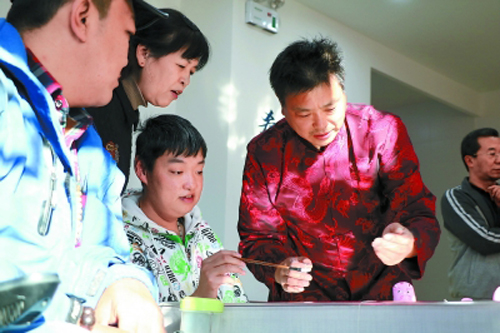 兔兒爺?shù)谖宕鷤魅藦堉覐?qiáng)(右一)正向馬鋼(左一)等殘疾人教授彩塑技藝。